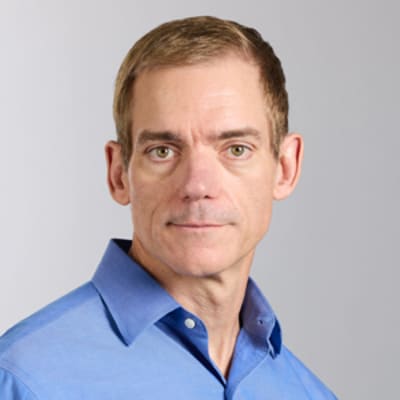 Bob McCarter with short light brown hair in a blue button-up shirt, looking at the camera. The background is plain and light-colored.