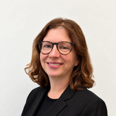 A woman with shoulder-length brown hair and glasses smiling against a plain white background.