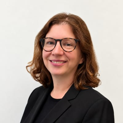 A woman with shoulder-length brown hair and glasses smiling against a plain white background.
