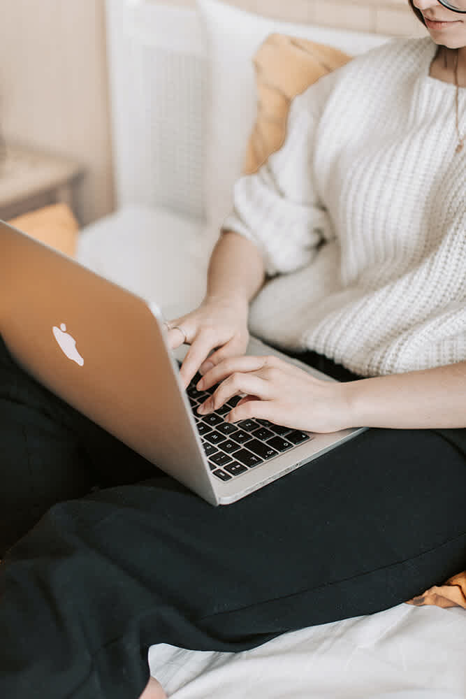 person in sweater typing on Apple laptop