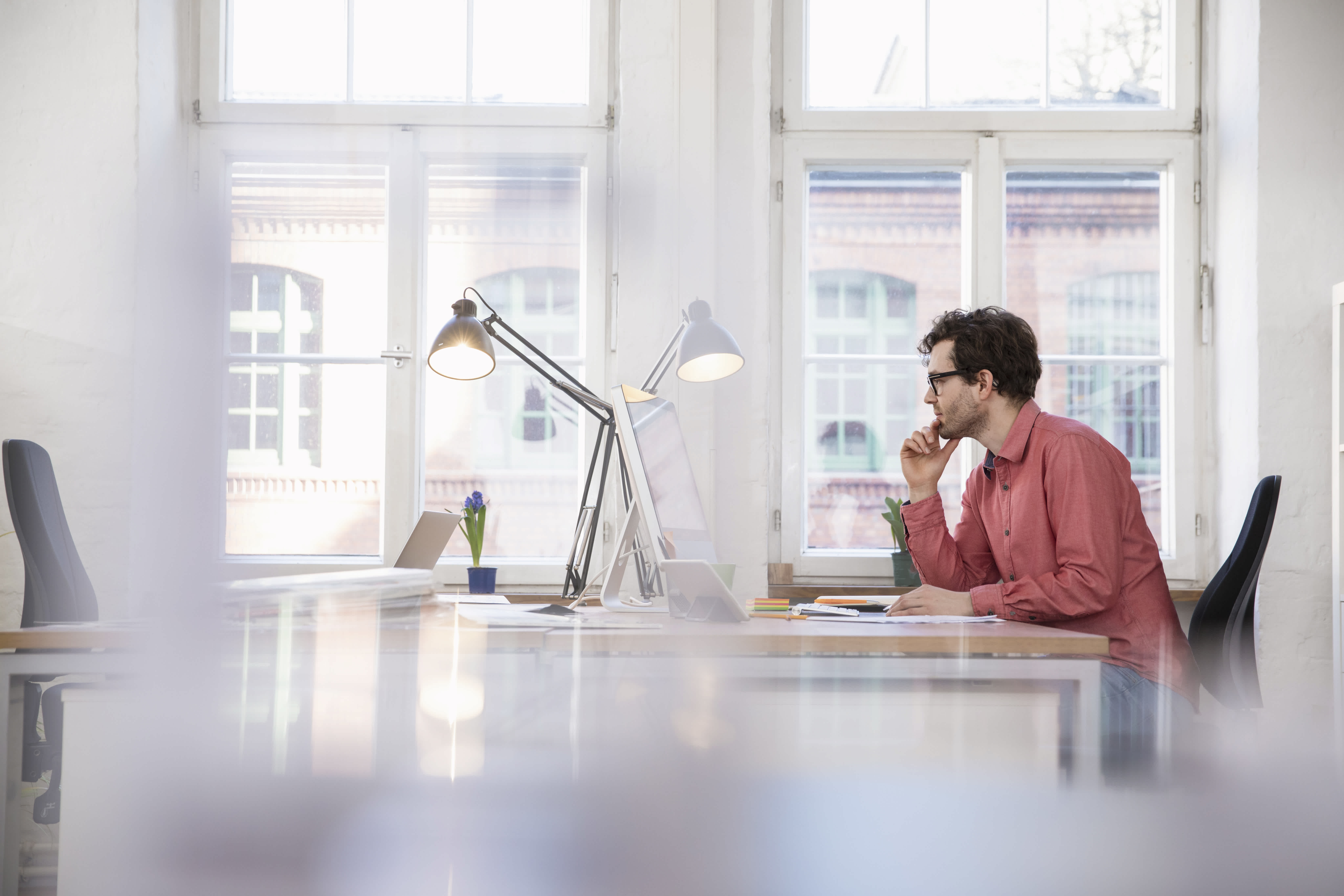 white man contemplating at his desk, in front of a window