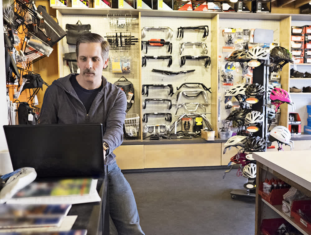 white man with a mustache in a hoodie working at a bike shop