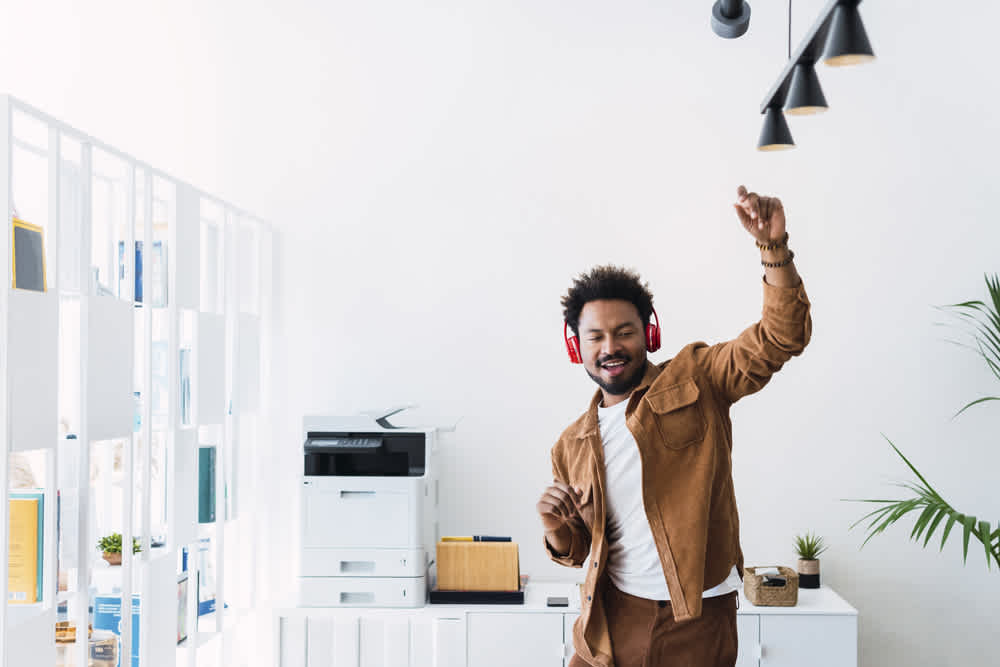 Black man in brown denim shirt dancing wearing headphones in a copy room