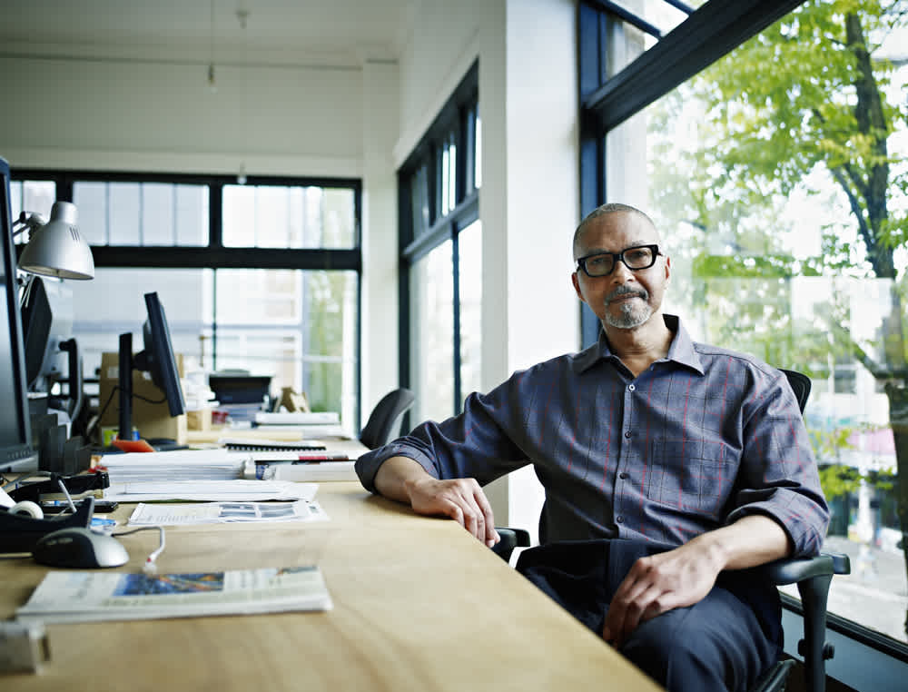man  in glasses sitting at a desk in open office by window