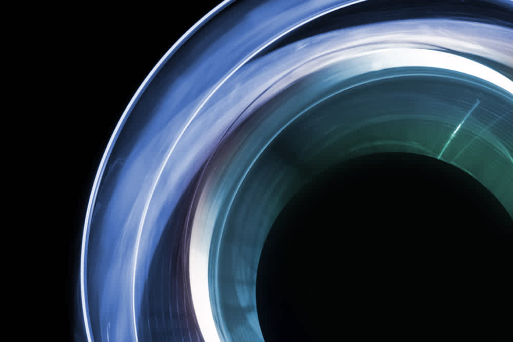 Abstract image featuring circular shapes in shades of blue, green, and white, set against a black background. The design resembles overlapping translucent rings with light reflections and a dark central area.