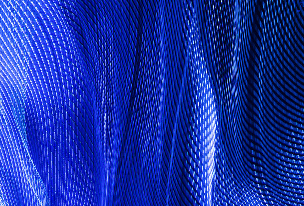 Abstract image featuring dynamic waves of blue lines and patterns on a dark background, creating a sense of movement and depth. The lines are tightly woven, resembling textiles or digital grids, with varying shades of blue highlighting texture.