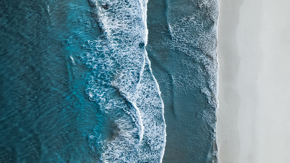 aerial view of waves breaking against white sand beach