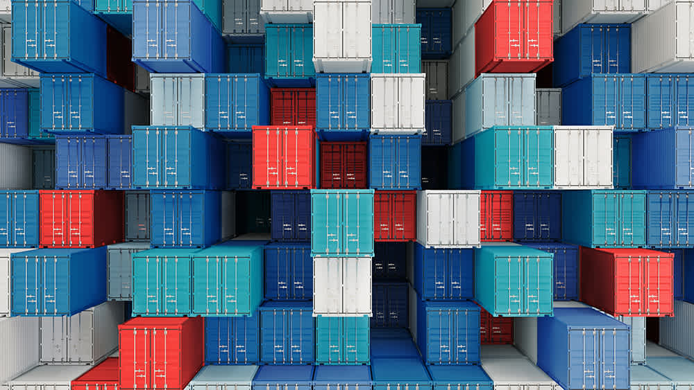 A large stack of interlocked shipping containers in various colors including blue, red, and white. The containers are arranged in a tightly packed, symmetrical pattern, resembling a geometric puzzle.