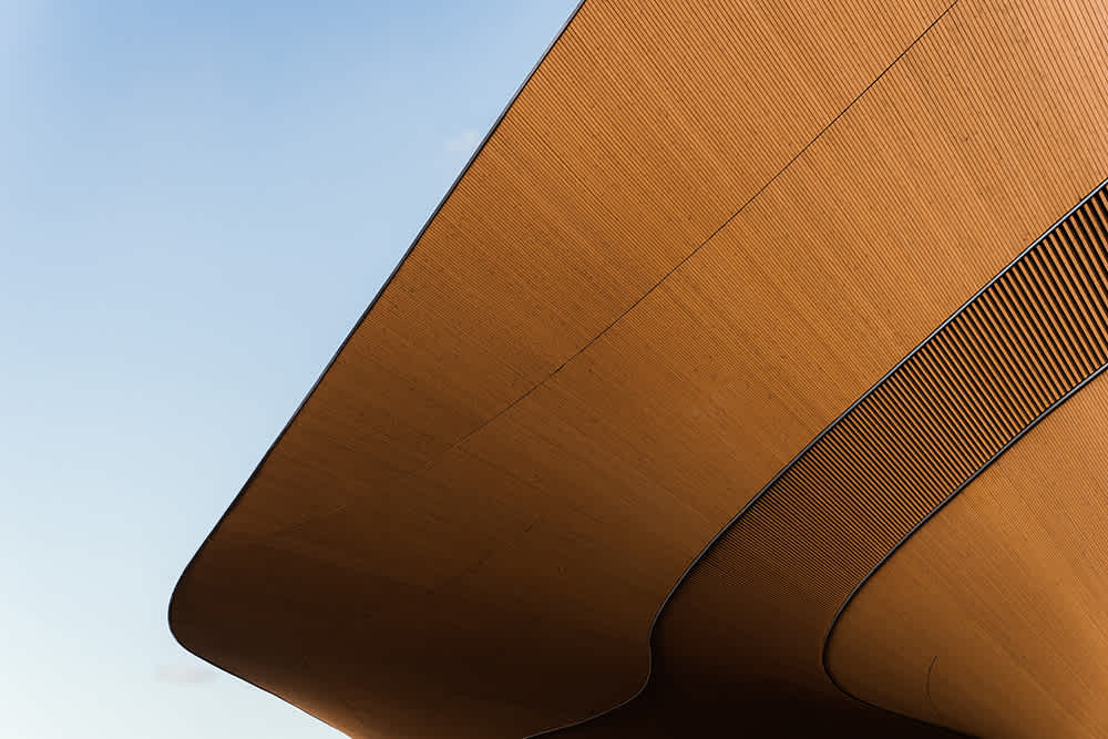 View underneath modern curved orange wood-paneled building against a clear blue sky