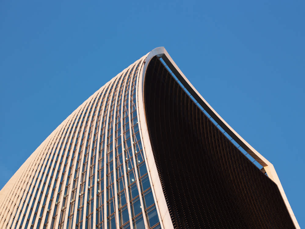 A modern skyscraper with a distinctive curved design against a clear blue sky. The building features a grid of windows and a smooth, sweeping architectural style.