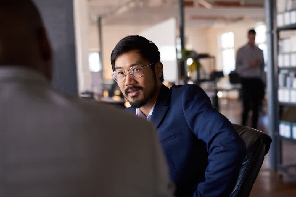 Two women in business attire smiling and looking at a laptop screen in a modern office setting, appearing to collaborate on a project.