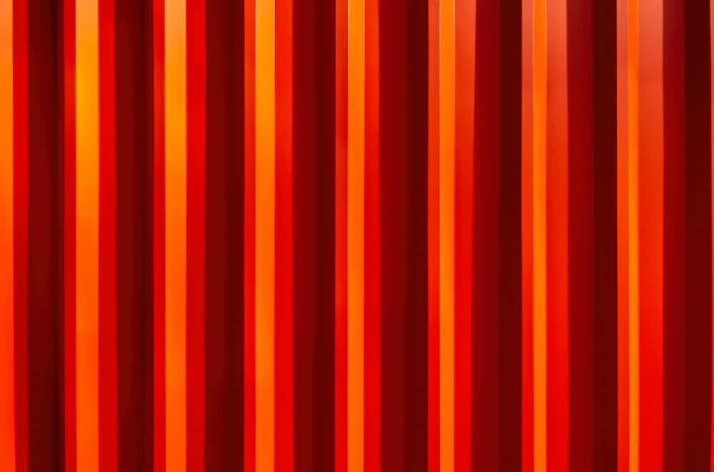 Vertical red and orange stripes with varying widths create an abstract, vibrant pattern resembling metal or painted panels.
