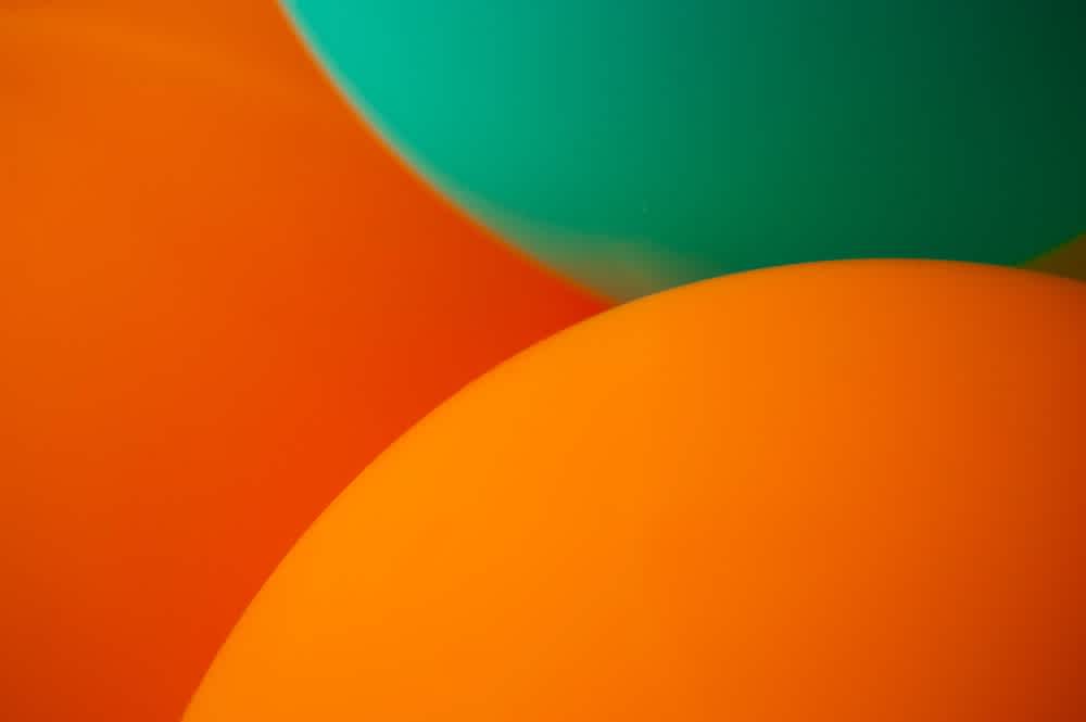 Close-up of three balloons, two orange and one teal, overlapping each other to create a colorful and festive abstract pattern.