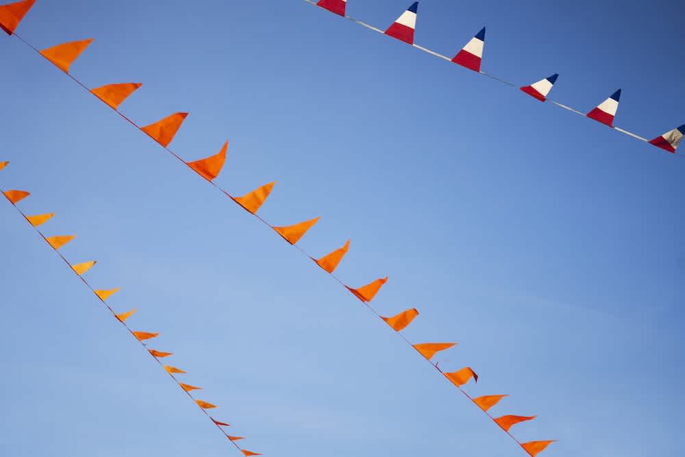 Orange triangular pennant flags and red, white, and blue patterned flags hang from strings against a clear blue sky.