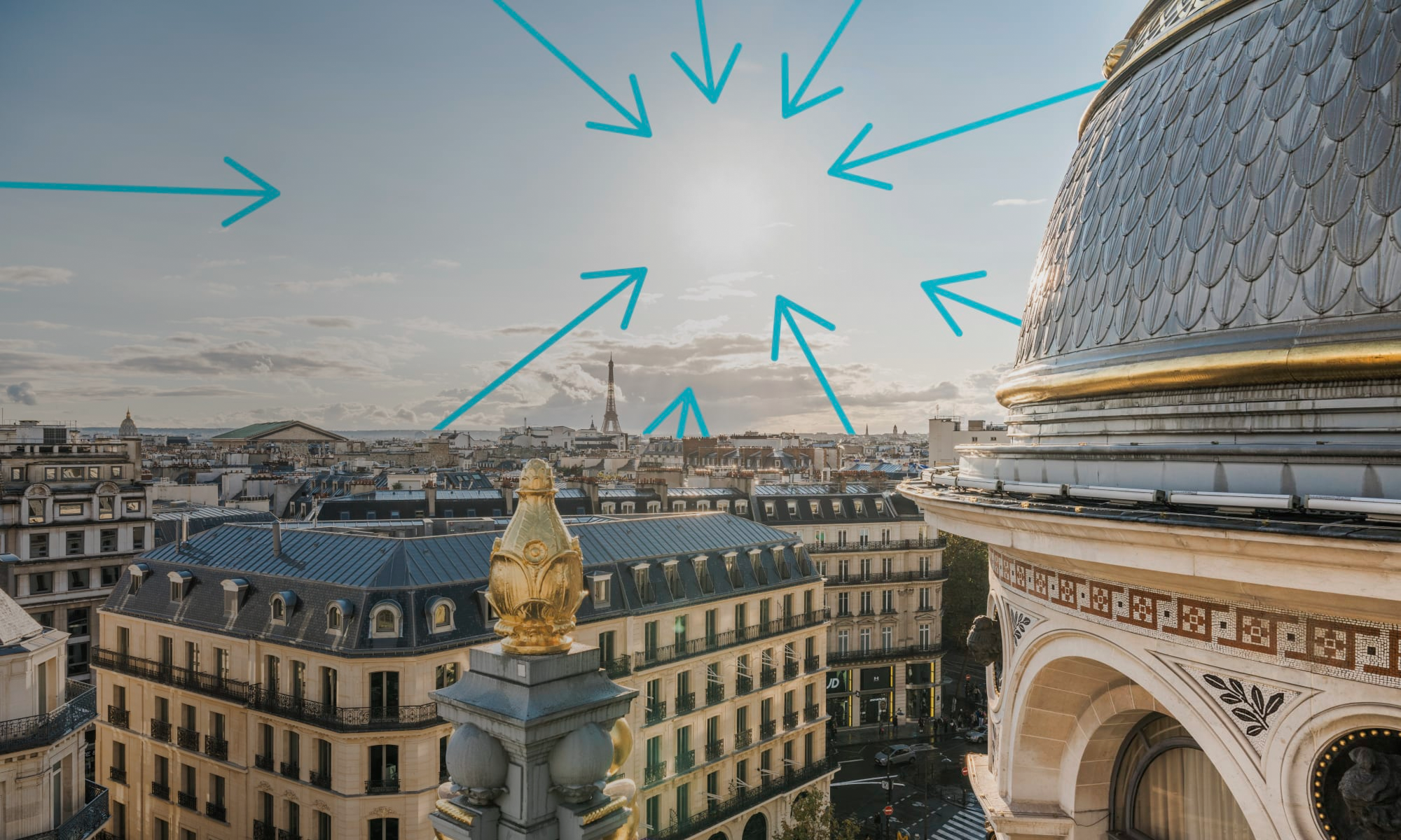 View of Paris rooftops and historic buildings at sunset, with blue arrows digitally pointing toward the sun in the sky; ornate dome and golden statue in the foreground.