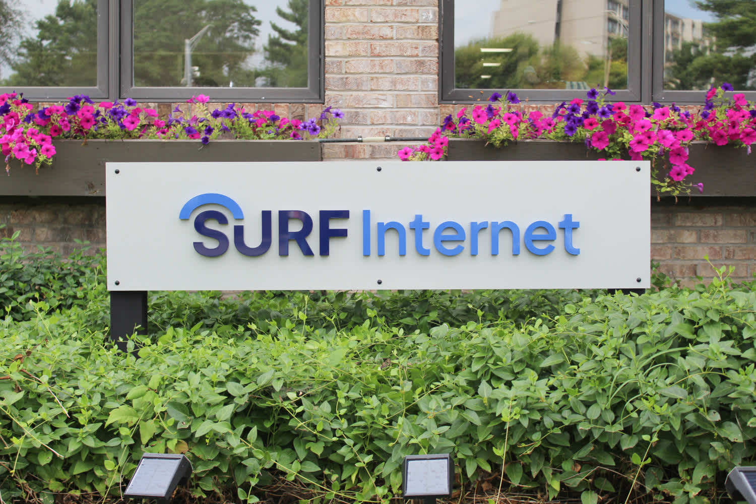 A close-up view of a modern glass office building at dusk, showing several floors with illuminated windows, revealing desks, chairs, and office equipment inside.