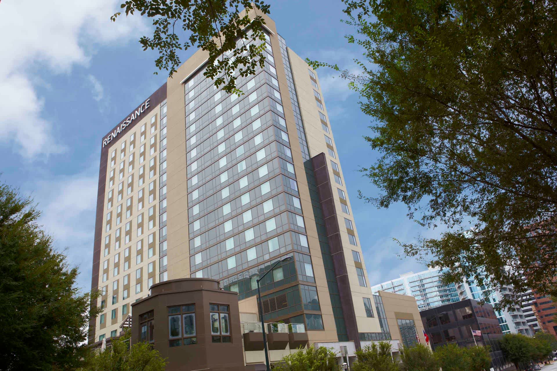 A tall modern hotel building with the sign RENAISSANCE at the top, surrounded by trees and city buildings under a partly cloudy sky.