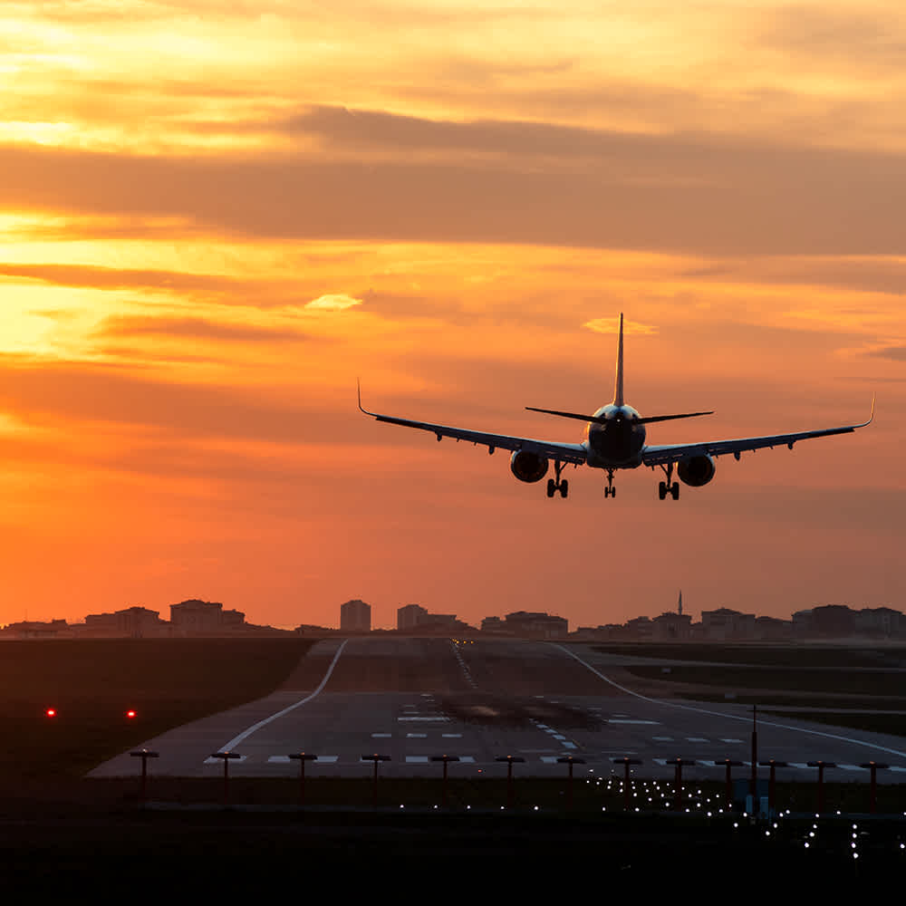 A person dressed in a brown jacket and a striped shirt is holding and using a smartphone, with the focus on their hands and phone, and the background blurred.