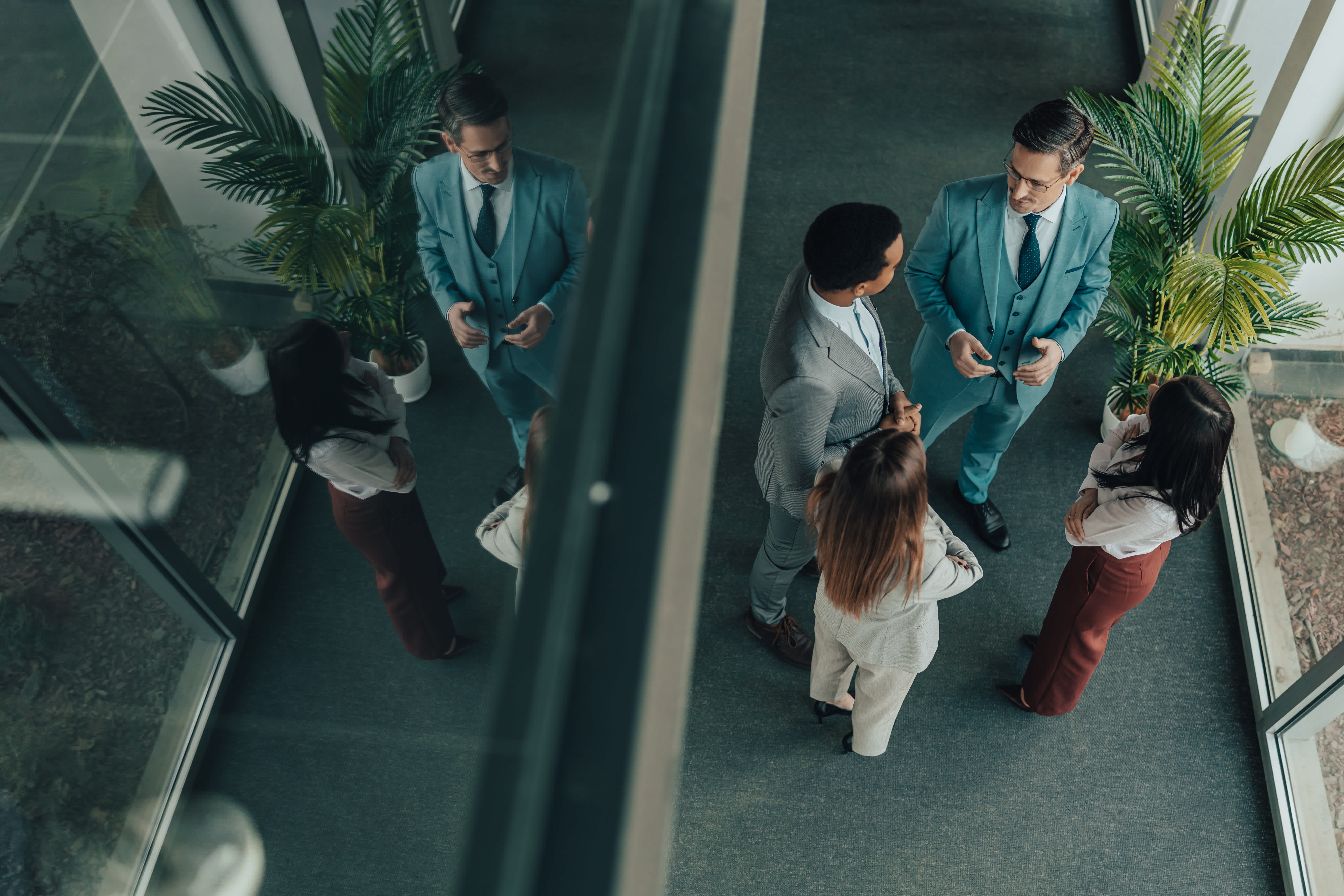 Group of business professionals standing in an office corridor and discussing work from an overhead perspective.