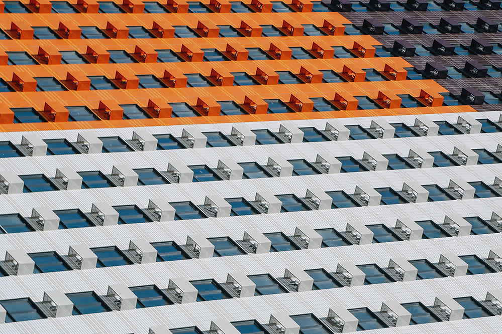 Rows of rectangular windows on a modern building, with alternating bands of orange, gray, and white panels, creating a bold geometric pattern.