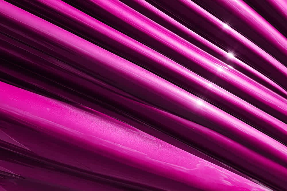 Close-up of vibrant, magenta-colored, diagonal lines with a shiny, reflective surface and soft highlights. The image has an abstract, modern feel.