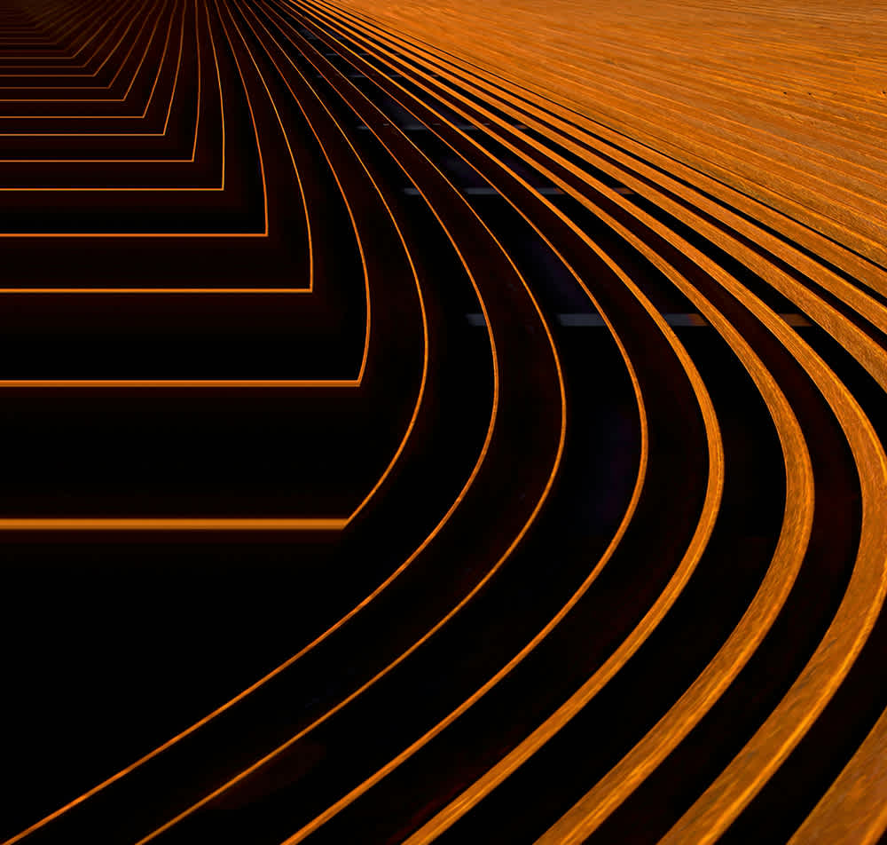 Abstract image featuring curved and straight orange lines on a black background, creating a dynamic pattern resembling waves or tracks that converge and bend toward the upper left corner.