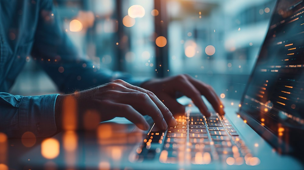 Hands typing on a laptop keyboard with colorful lights and blurred code lines, creating a futuristic, technology-focused atmosphere.