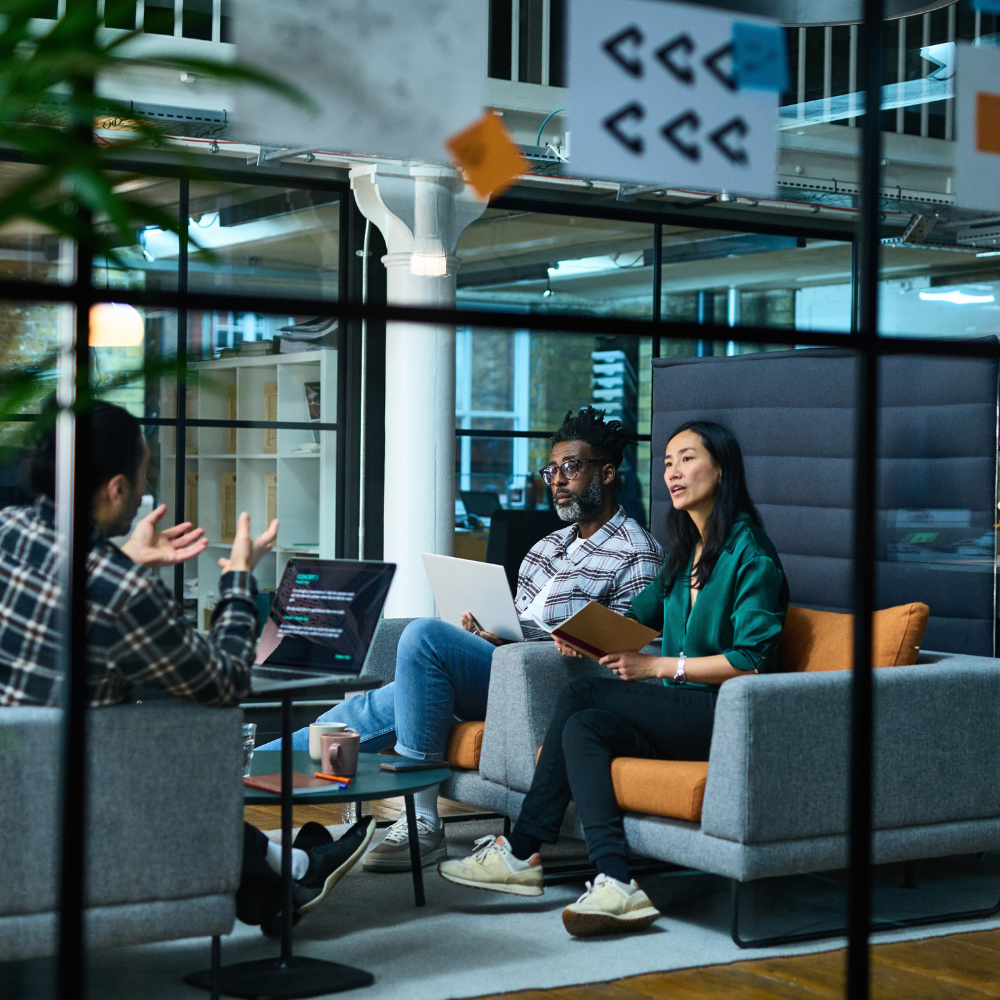Three colleagues in a https://cdn.navex.com/image/upload/Three colleagues having a meeting in an office lounge area with two people seated on sofas and one person seated in a chair facing them./new-navex-brand-2023/people/Why_attend_image.pngoffice meeting, seen through a glass partition with sticky notes attached.