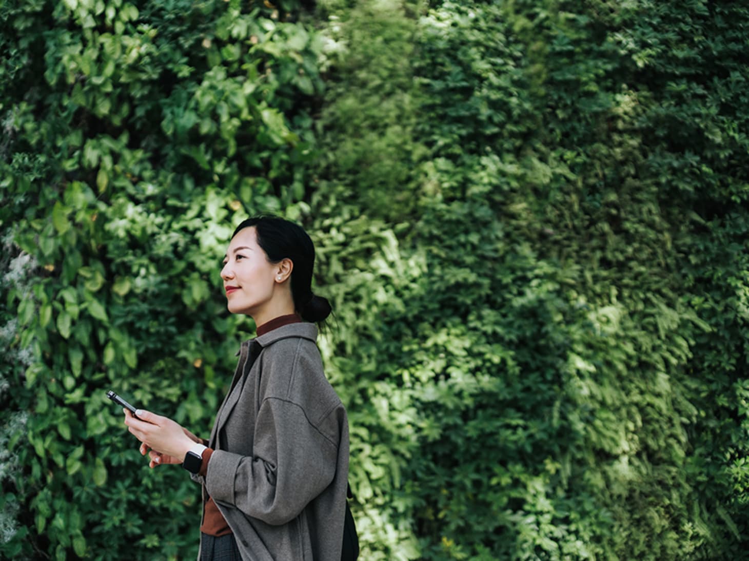 Asian woman walking with phone in front of greenery 