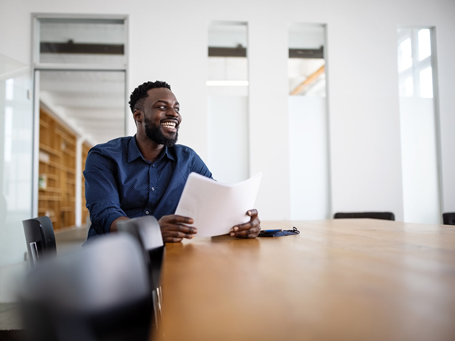 black man smiling, sitting alone at a conference table 