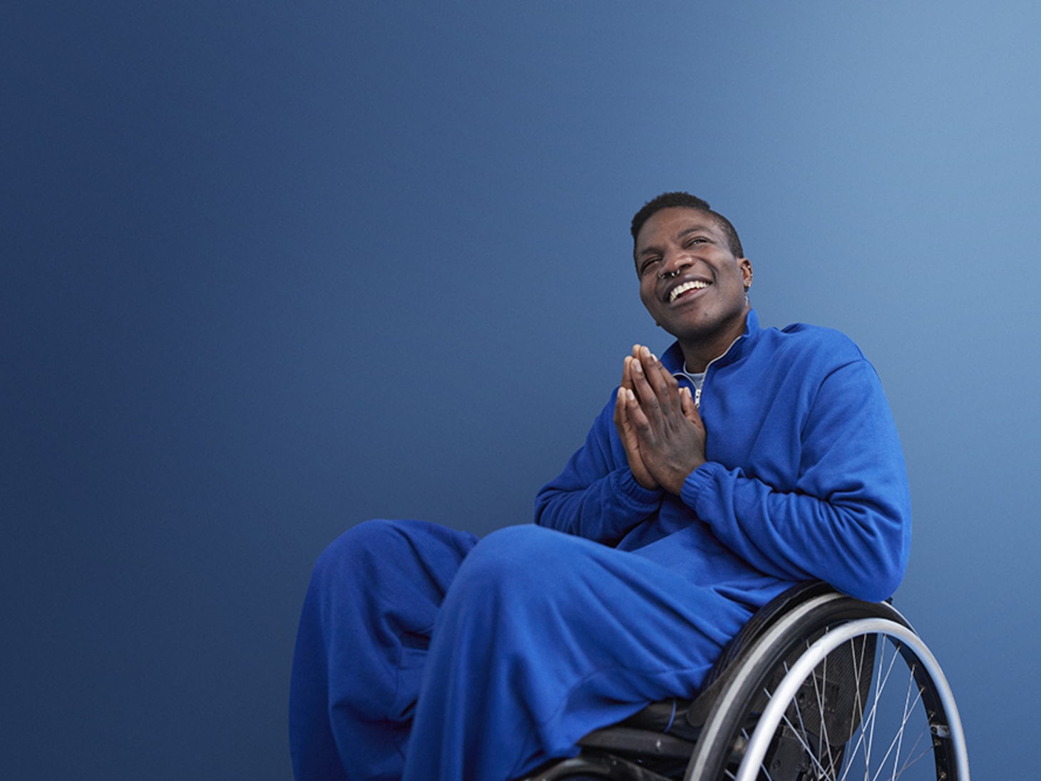 black man in blue, blue background, sitting in a wheelchair