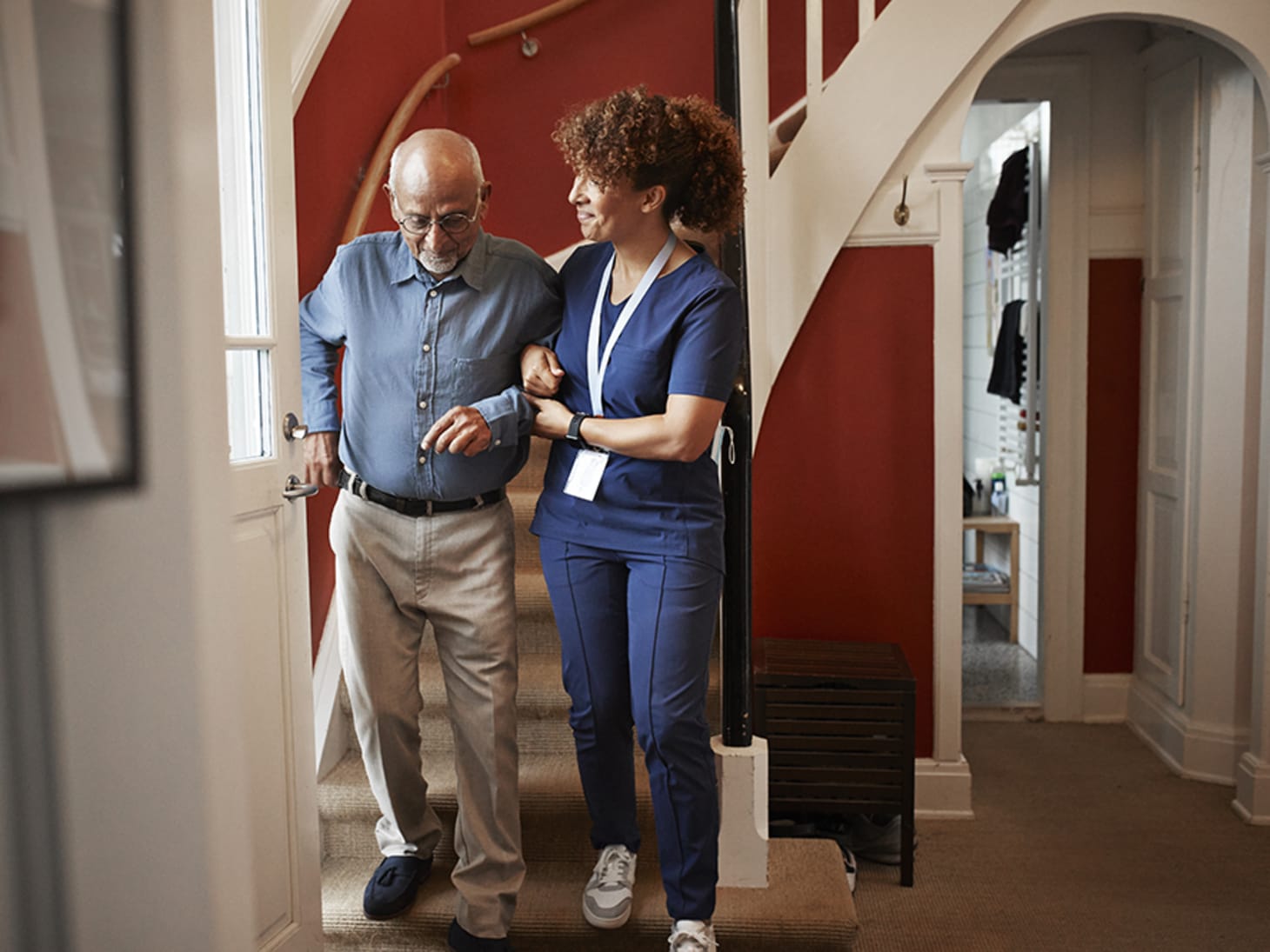 female home aid supporting an elderly man walking down stairs 