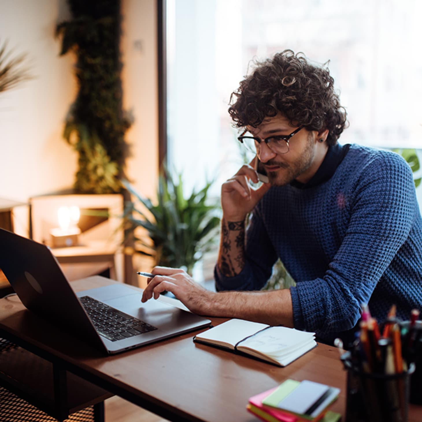 man with curly hair talking on phone while at home office