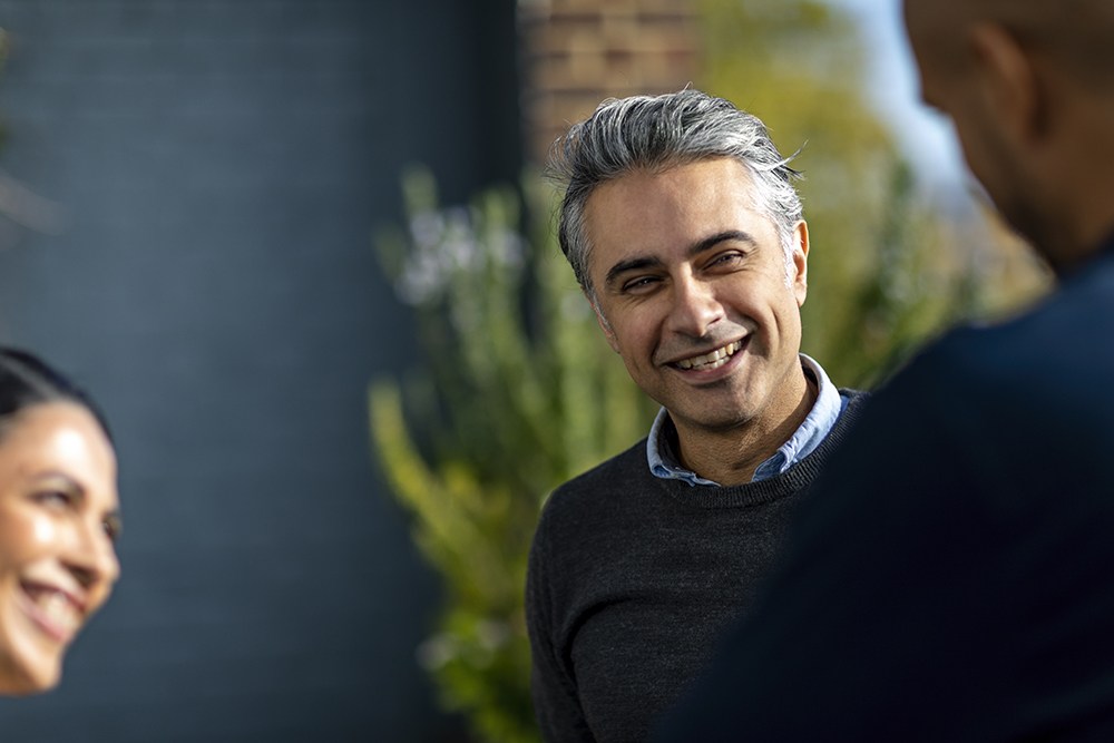 man with gray hair in sweater talking with coworkers