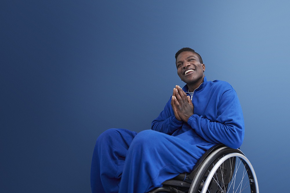 black man in blue, blue background, sitting in a wheelchair