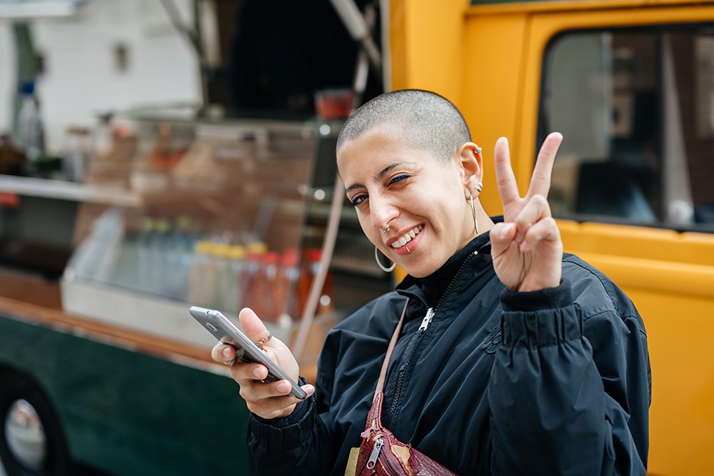 white woman with shaved head and piercings, showing peace sign