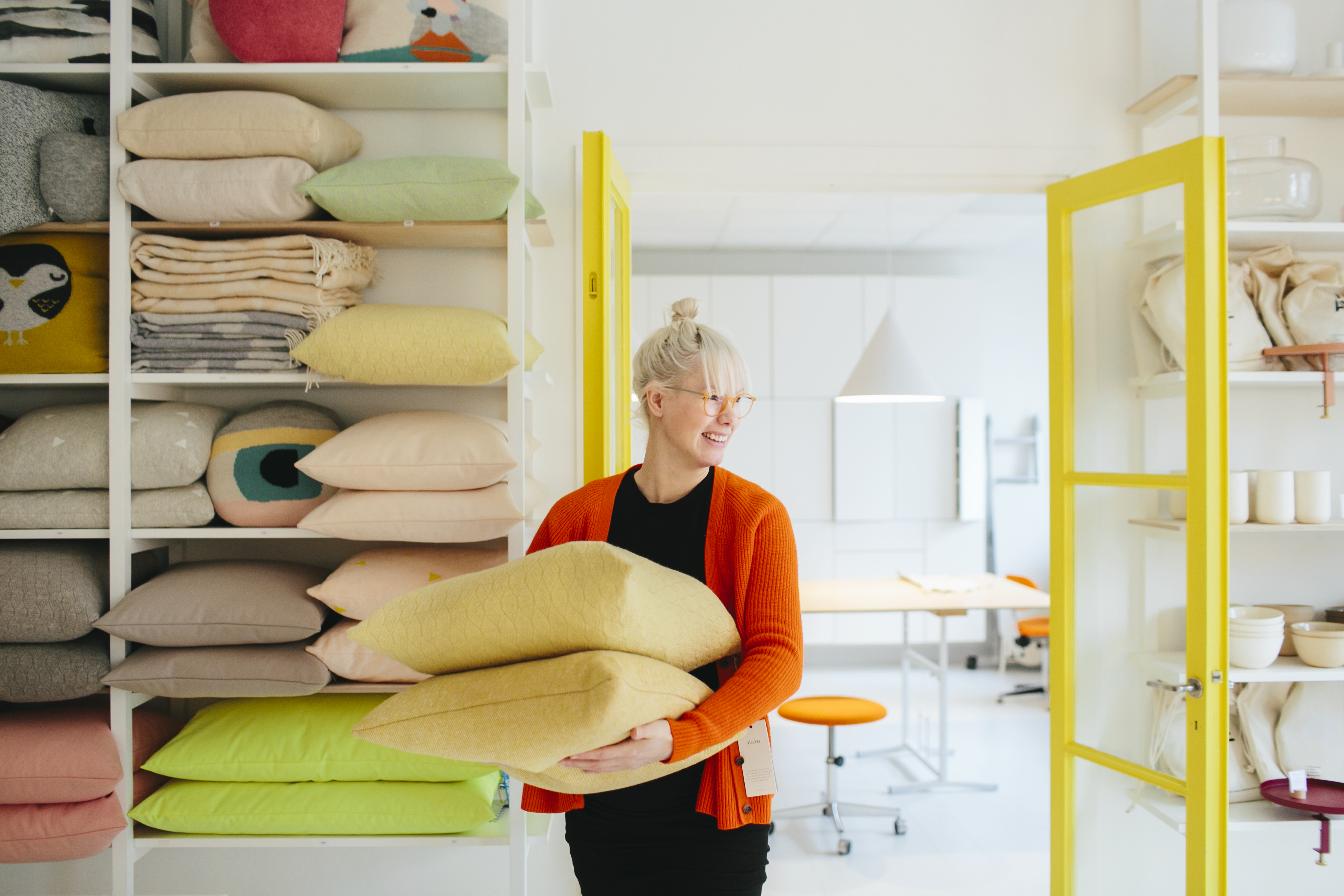 blonde woman in black with an orange sweater, working at a homegoods store