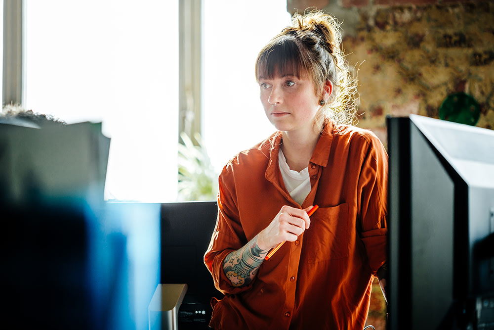 white woman with auburn hair and an orange shirt standing at her computer desk