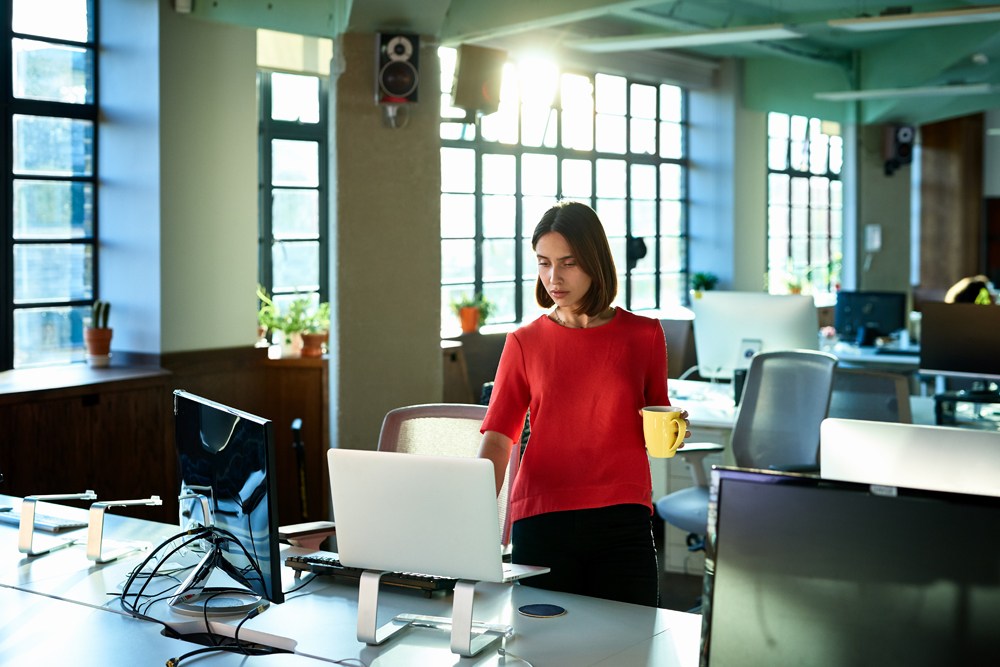 woman in red shirt holding mug standing at desk in empty office