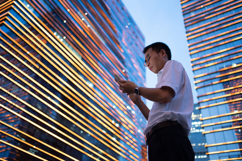 Asian man on cell phone outside two skyscrapers