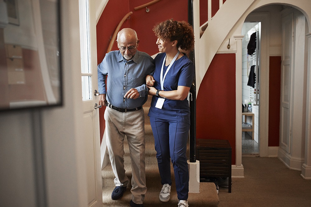 female home aid supporting an elderly man walking down stairs 