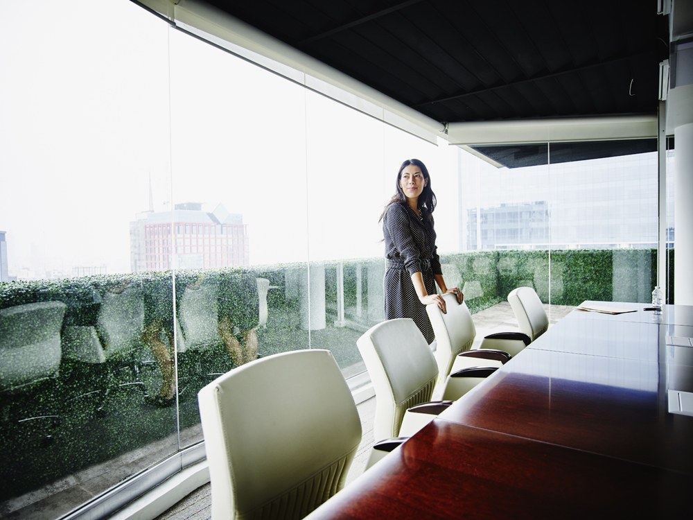 woman standing against chair at conference table in empty room with glass walls behind