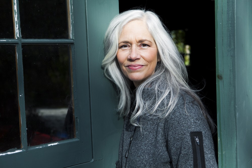 midaged white woman with long silver hair standing in a dark teal doorway