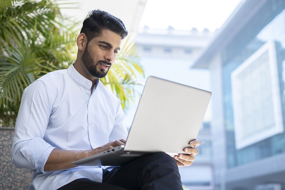 Indian man in nice shirt working on his computer in front of a plant