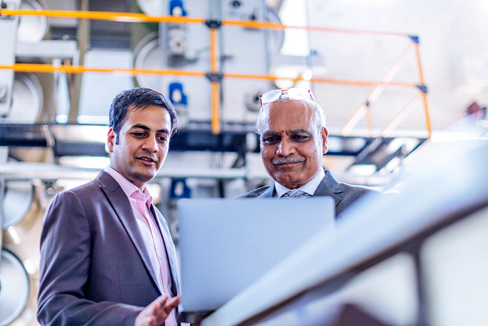 two Indian men working on a laptop in a manufacturing facility