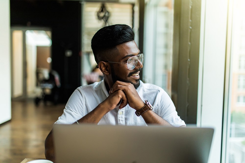 Indian man in glasses working at his laptop by the window