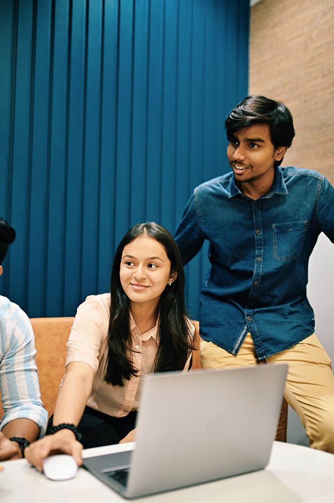 male and female Indian colleagues working at a table and talking with others