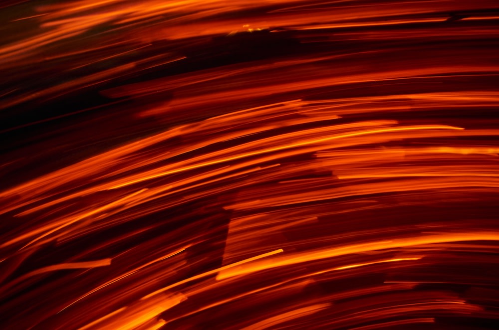 Swirling streaks of bright orange and red light create an abstract, dynamic pattern against a dark background, suggesting motion and energy.