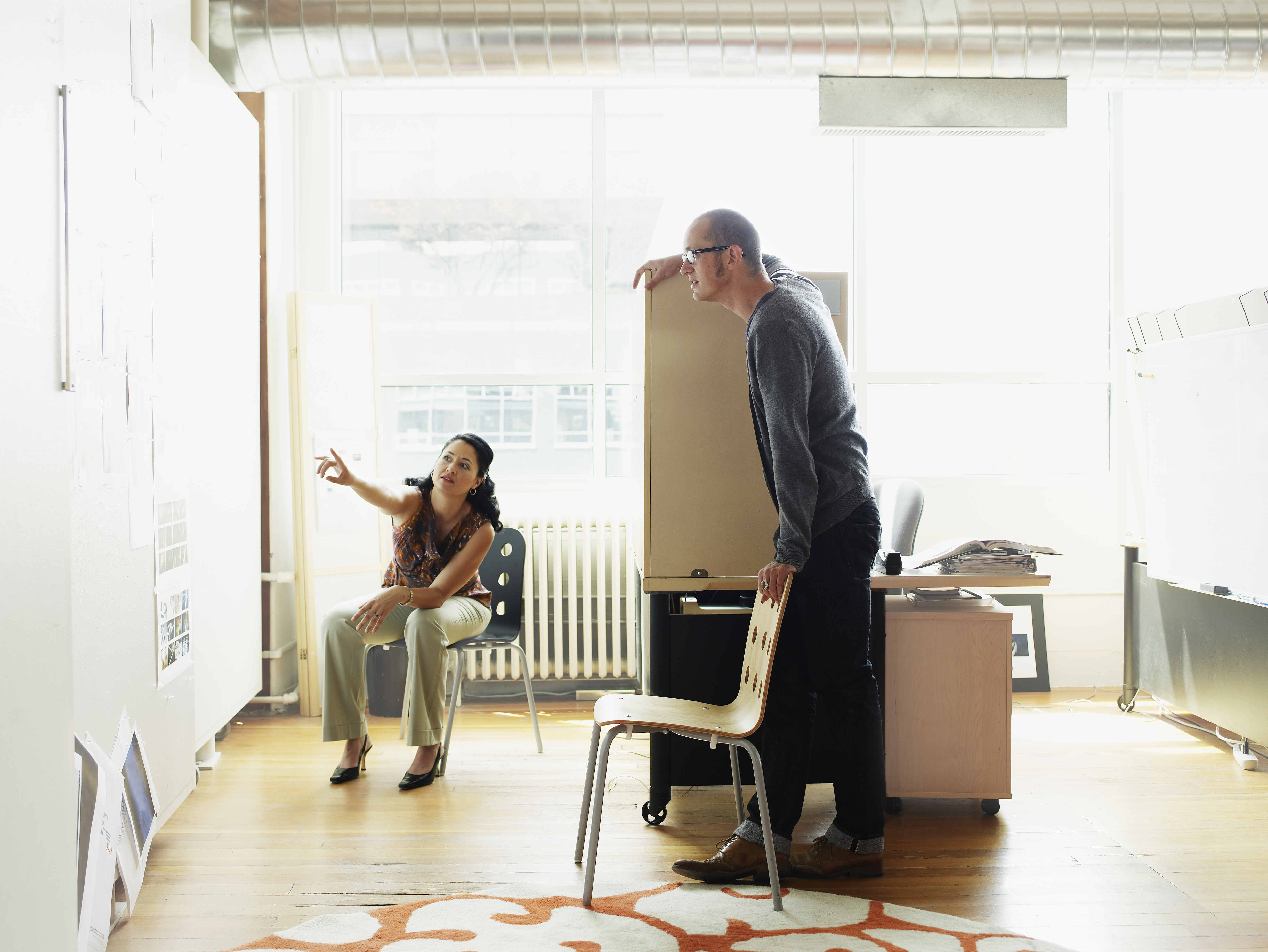 man and woman in office, woman pointing out details on whiteboard to man 