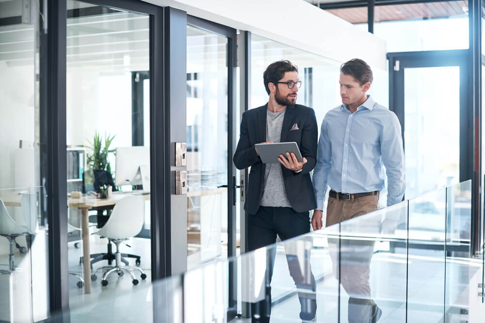 two male presenting colleagues walking down office hall together 